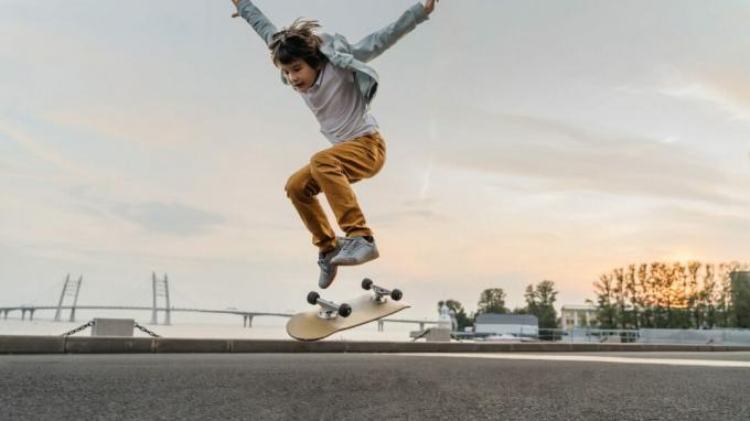 Pojkehoppning på skateboard på gatan. Rolig ungeskridskoåkare som övar ollie på skateboard vid solnedgången.