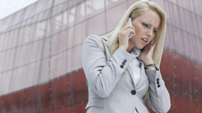 Kvinna med ADHD lyssnar på någon i mobiltelefonen och blir arg framför den höga byggnaden